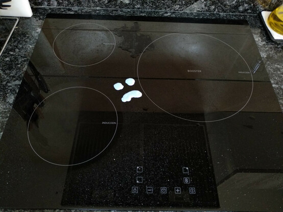 Fotografia d’una placa d’inducció amb un dibuix d’una cara trista fet amb producte de neteja.