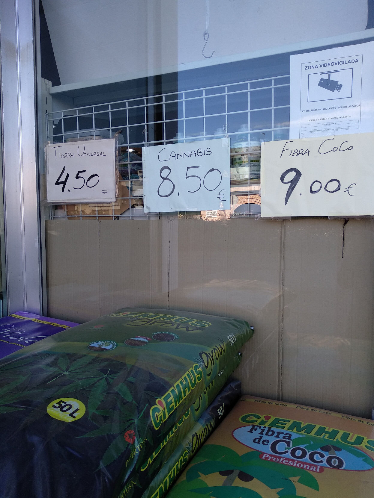 Aparador d'una tenda amb sacs de terra. En un dels cartells es pot llegir: 'Cannabis 8,50 €'.