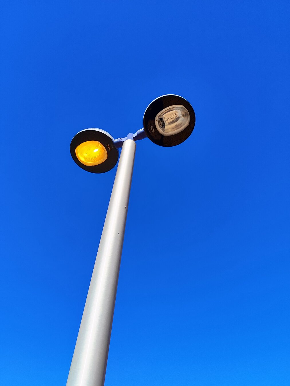 Fanals dobles vistos des de baix, amb un llum encés i un altre apagat. Al fons, un cel blau intens.