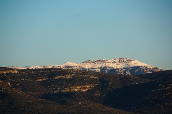 Paisatge de muntanya amb cims parcialment coberts de neu, contrastant amb les zones més baixes de tons verds i terrosos. El cel és ras i blau.
