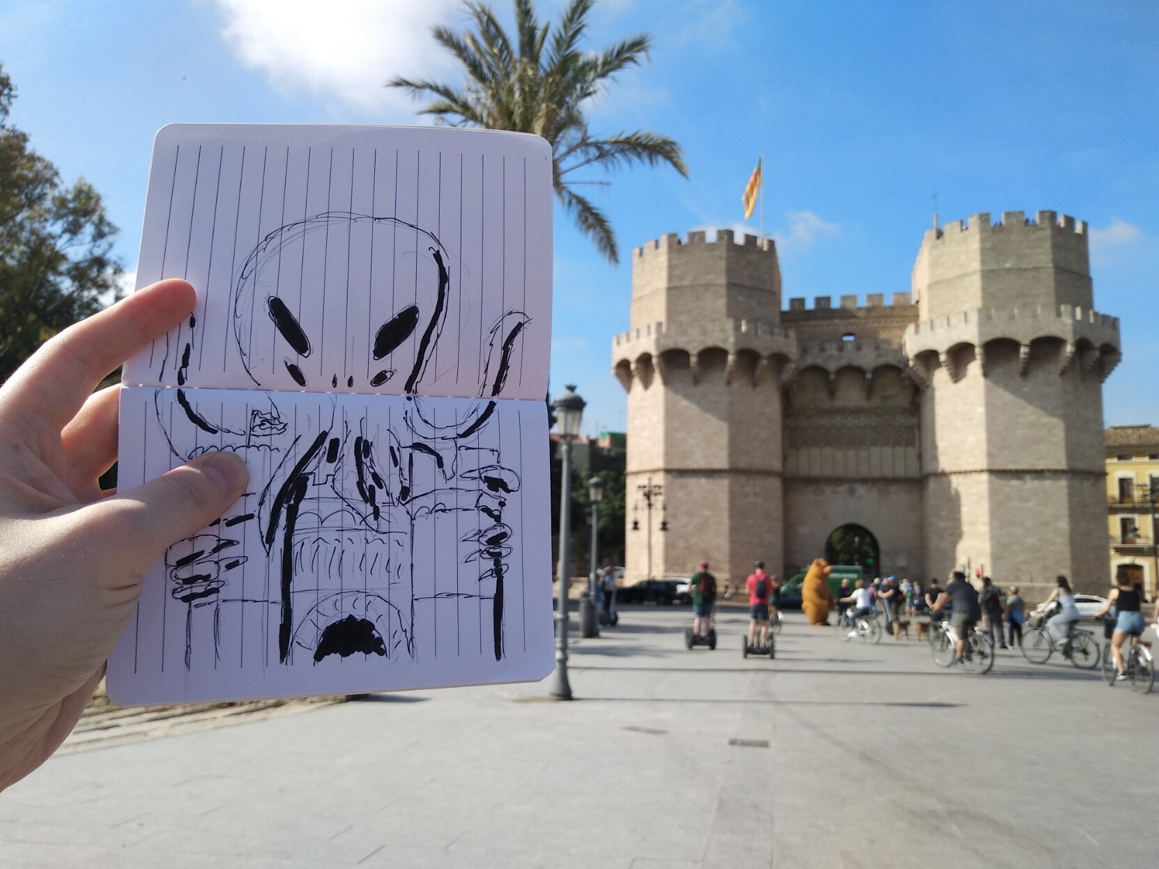 En primer pla, una llibreta oberta amb una il·lustració d'un monstre sobre les torres dels Serrans. En segon pla, les torres dels Serrans.